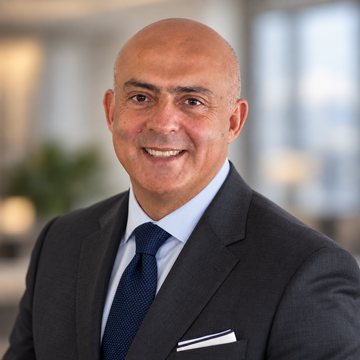 José Salloum, conseiller en sécurité financière, en complet anthracite et cravate marine avec pince, une pièce éclairée derrière lui