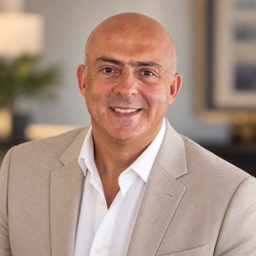José Salloum, conseiller en sécurité financière, en veston beige et chemise blanche ouverte, un tableau encadré derrière lui