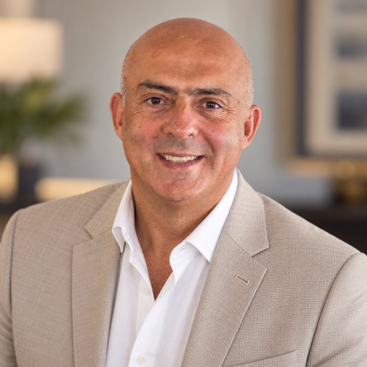 Jose Salloum, Infinite Banking practitioner, in a tan jacket and an open white shirt, a framed picture behind him