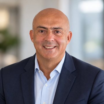 Jose Salloum, Infinite Banking practitioner, in a navy suit and an open light blue shirt, a framed picture behind him