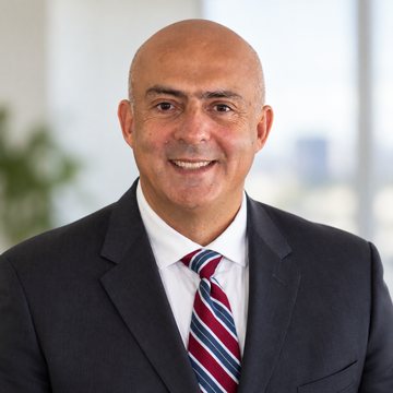 Jose Salloum, Infinite Banking practitioner, in a charcoal suit and a burgundy striped tie beside a green plant