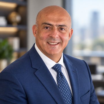 Jose Salloum, Infinite Banking practitioner, in a navy suit and a patterned tie beside a bookcase and a city window