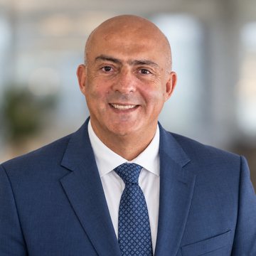 Jose Salloum, Infinite Banking practitioner, in a navy suit and a navy patterned tie in a pale daylit office