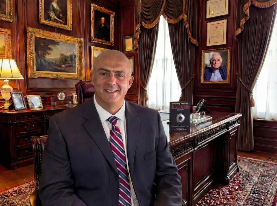 Jose Salloum assis à un bureau dans un bureau lambrissé. Un exemplaire de Becoming Your Own Banker et un portrait encadré de R. Nelson Nash sont visibles derrière lui.